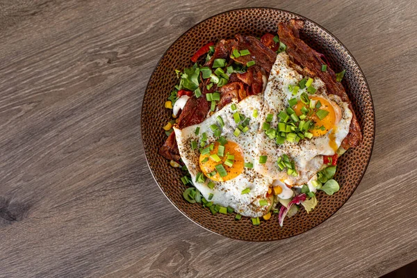 Tasty, yummy fried egg, scrambled egg, with meat and bacon with green grocery and corn on plate on the table in cafe. Greasy, unhealthy dish. Fast food and snacks. Flat lay, top view, copy space.