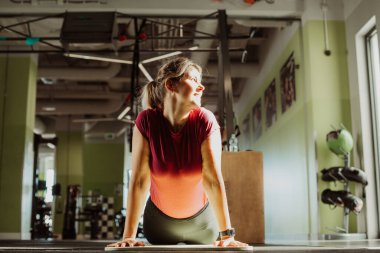 Ayrıca beden eğitimi dersinde kolları minderde destekle karın üstü yatar ve gülümseyerek başını çevirir. Genç kadın esneme egzersizi yapıyor. Spor merkezinde eğitim, jimnastik, yoga, yaşam tarzı.