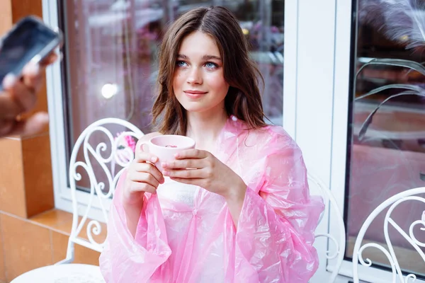 Csinos Mosolygós Lány Esőkabátban Széken Kint Kávézóban Élvezi Rózsaszín Csészéből — Stock Fotó