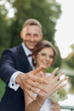 Dışarıda dikilen, yazın parkta kucaklaşan altın nişan yüzüklerini gösteren mutlu bir çiftin portresi. İlişki, aşk. Seçici odak, dikey.