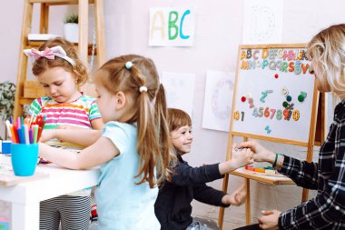 Çocuklu kadın öğretmen çocuk gelişim merkezinde eğleniyor. Resim, sanat, matematik ve İngilizce dersleri. Koruyucu aileler, evlat edinme ve çocuk bakımı için anaokulu ve erken eğitim.
