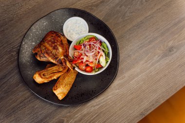 Lezzetli kızarmış ördek, sebze salatası, salatalık, yeşillik, domates ve soğanlı puf böreği ve siyah taş tabakta krema sosu, restorandaki ahşap masada. Üst görünüm, alanı kopyala