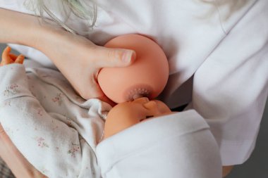Kadın göğüslerinin ve oyuncak bebeklerin el ele tutuşma fotoğrafı. Nitelikli bir öğretim görevlisinden hamile kadınlar için eğitim. Çevrimiçi çalışma, emzirme, beslenme, emzirme, yeni doğanların bakımı.