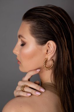 Dikey yakın plan, zarif, modaya uygun esmer kadın profili kapalı gözler, profesyonel makyaj, gri arka planda altın aksesuarlar. Mücevher hediye bayramı. Lüks vintage tasarım süsü