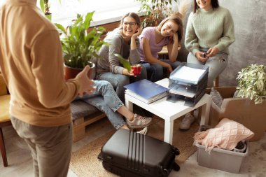 Pozitif, neşeli, gülen, aktif, oyuncu kız öğrencilerin toplanıp oturma odasındaki eşyaları paketlemelerine yardım etmesi. Yeni akademik yıl için yeni kampüse taşınacağız. Üniversite ya da üniversite