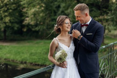 Yazın parktaki köprünün üzerinde duran gülen bir çiftin portresi. Genç ve çekici bir kadın nedime buketi tutuyor, genç damat elini uzatıp gelini okşuyor. İlişki, aşk.