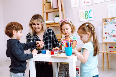 Çocuklu kadın öğretmen, anaokulu için çocuk gelişim merkezinde eğleniyor, oyunlar oynuyor, alfabe ve numaralar öğreniyor. Özel okul merkezinde kreş ve bebek bakıcılığı