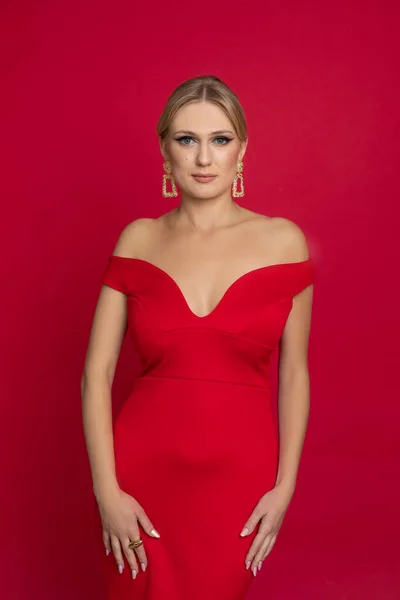 垂直方向の自信を持って 魅力的な ポッシュ アクセサリー 深い低首のドレスを持つエレガントなブロンドの女性は 赤いスタジオの背景にカメラを見てください 赤で女性のためのイベントのお祝いの服 スペースのコピー — ストック写真