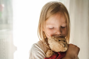 Sarı saçlı küçük kız nazikçe en sevdiği yumuşak oyuncağına sarıldı. Oyuncak ayılı kız. Oyuncak Ayı ve Çocuk