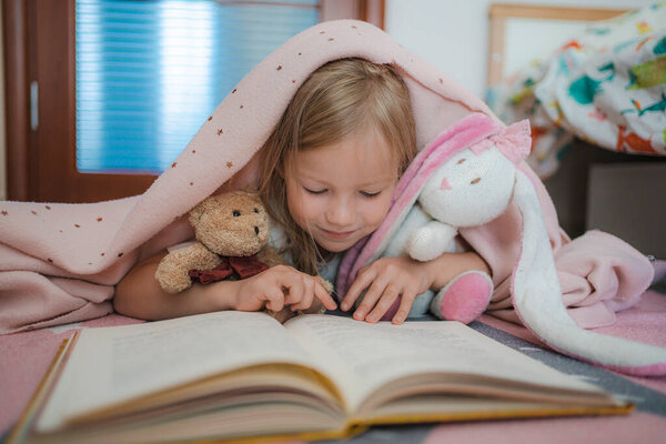 Маленькая девочка в розовой детской читает книгу. уютная детская комната с игрушками. комната для девочек
