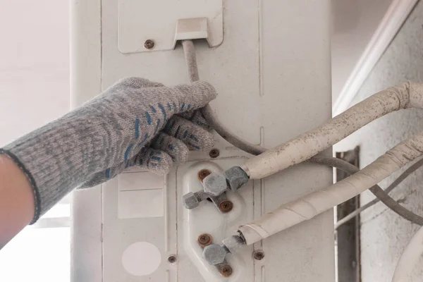 The hand of an air conditioner repair and maintenance specialist in a construction glove working with air-conditioned old equipment.