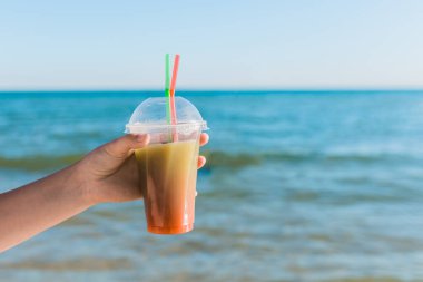Adamın eli denizin arka planında renkli, soğuk, alkolsüz bir kokteyl tutuyor..