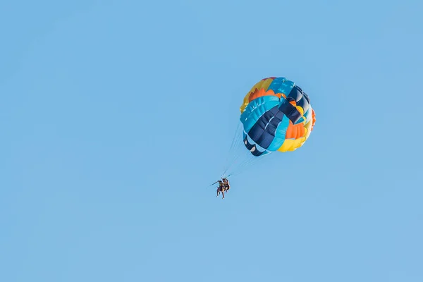 Extreme sports and exciting rest activity. Vacationing tourists fly on a parashute in blue sky background.