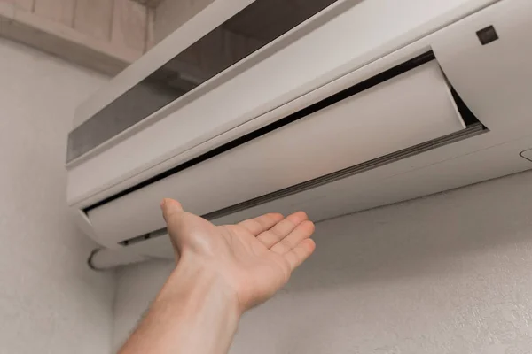 温度や暖かい空気や冷たい空気の感じを確認するために部屋にエアコンの下に手を置きます — ストック写真