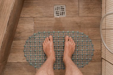 Men's feet stand on a plastic anti-slip mat next to the floor drain in the bathroom or shower. clipart