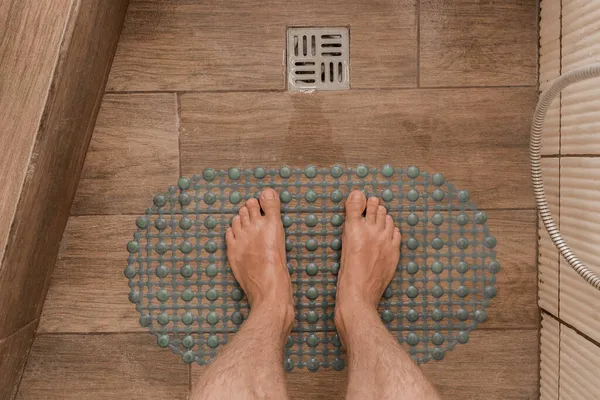 Men\'s feet stand on a plastic anti-slip mat next to the floor drain in the bathroom or shower.