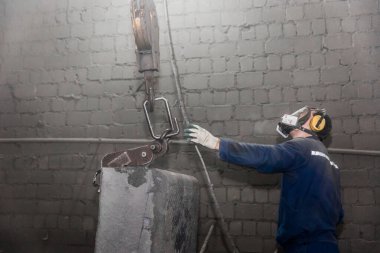 Tulumlu ve solunum cihazlı bir işçi, el kaldırma mekanizması ile bir kanca alır. Bir endüstriyel fabrikanın atölyesinde demir takviyeli beton borular..