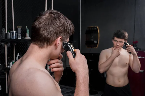 裸の胴を持つ人は 鏡の前に電気機械で黒い髪を切ります 家の外観のケア — ストック写真