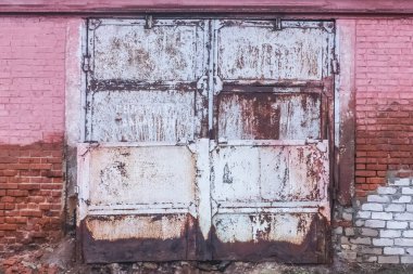 Eski kirli, yıpranmış demir bir depo kapısı ve terk edilmiş binalardan oluşan tuğla bir duvar..