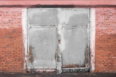 Eski kirli, yıpranmış demir bir depo kapısı ve terk edilmiş binalardan oluşan tuğla bir duvar..