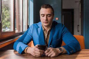 İş adamı, beyaz takım elbiseli, şık, yakışıklı bir adam, kafeterya arka planındaki bir masada, akıllı bir telefon ya da cep telefonuyla vakit geçiriyor..