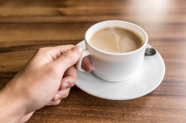 Bir adam kahve fincanında bir fincan kahve alır ve elini bir kafedeki ahşap bir masanın arka planına koyar..