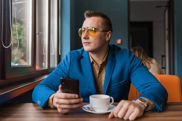 유럽에서 선글라스를 사업가 시간에 테이블에 스마트폰이나 전화를 내다본다 — 스톡 사진