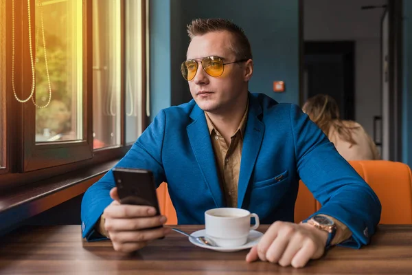 출신의 사업가가 선글라스를 휴게실에 탁자에 앉아서 스마트폰을 창밖을 내다본다 — 스톡 사진