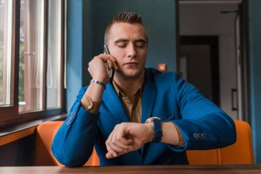 Ceketli bir işadamının Avrupalı gibi görünen bir portresi cep telefonu ya da akıllı telefonuyla konuşur ve bir kafede saatine bakar..