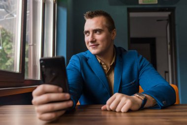 Pozitif, Avrupa görünümlü genç bir adam, şık bir iş adamı, pencereye bakar ve cep telefonu ya da akıllı telefon kullanarak selfie çeker..