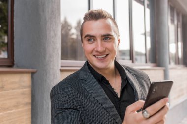 Kafkasyalı gülümseyen, neşeli bir adamın portresi ceketli ve gömlekli bir iş adamının açık havada elinde cep telefonuyla görüntüsü..