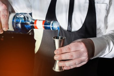 Profesyonel bir barmenin eli jigger kokteyline ya da ölçü kabına eklenen malzemeleri kontrol etmek için bir alete mavi şurup döker. Bir kokteyl hazırlama süreci.