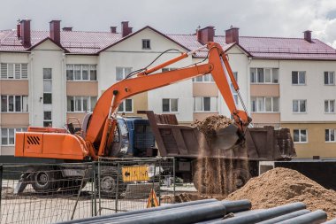Kazı işe yarıyor. Traktörün kovası toprağı inşaat alanındaki bir çöp kamyonunun arkasına kürekle dolduruyor..