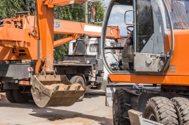 Kazı işe yarıyor. Bir traktör kovası, inşaat sahasındaki endüstriyel bir makinenin arka planına ağır bir kürekle kum zemini boşaltır..