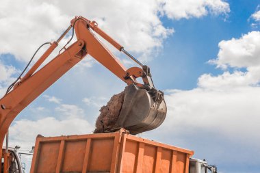 Kazı işe yarıyor. Traktörün kovası toprağı inşaat alanındaki bir çöp kamyonunun arkasına kürekle dolduruyor..