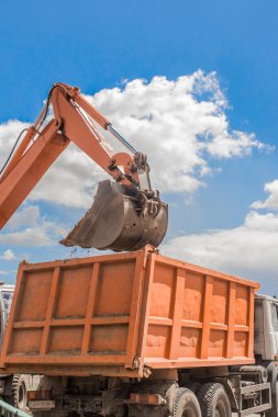 Kazı işe yarıyor. Traktörün kovası toprağı inşaat alanındaki bir çöp kamyonunun arkasına kürekle dolduruyor..