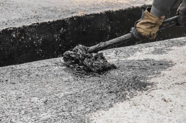 Bir inşaat işçisi, yapının beton yüzeyine siyah zift su geçirmez katranı tamir etmek ve uygulamak için pis bir el işi yapmakla meşgul..