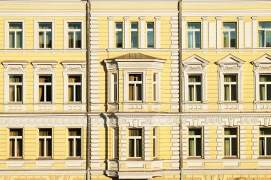 Arka planda çerçeveli pencereleri olan klasik mimari sarı bina cephesi. Eski bina cephesinin bir parçası.