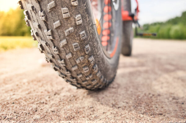 Close-up of fat mountain bike tire on dirty road. Fat bike wheel. Summer outdoor activity.