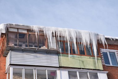 Balconies of an old residential brick house covered by the huge icicles. Dangerous icicles hangs from the roof. Harsh nord winter.