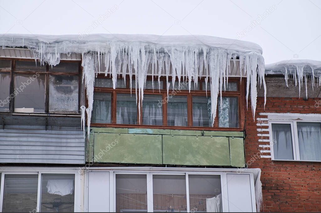 Balconies of an old residential brick house covered by the huge icicles. Dangerous icicles hangs from the roof. Harsh nord winter in the city.