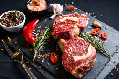 Baharatlı çiğ biftek ve siyah arka planda otlar. Tuz, biber, sarımsak, kırmızı biber ve biberiye.