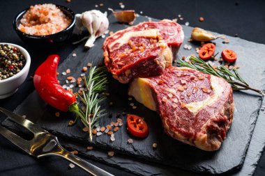 Baharatlı çiğ biftek ve siyah arka planda otlar. Tuz, biber, sarımsak, kırmızı biber ve biberiye.