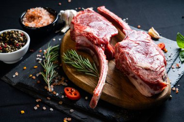 Baharatlı çiğ biftek ve siyah arka planda otlar. Tuz, biber, sarımsak, kırmızı biber ve biberiye. Kemikli çiğ et, en iyi biftek dilimleri.