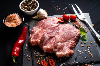 Baharatlı çiğ biftek ve siyah arka planda otlar. Tuz, biber, sarımsak, kırmızı biber ve fesleğen yaprağı.