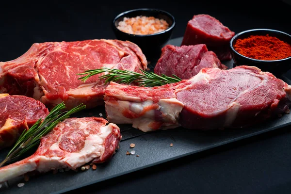 Filetes Carne Cruda Con Sal Especias Hierbas Sobre Fondo Negro Imagen de archivo