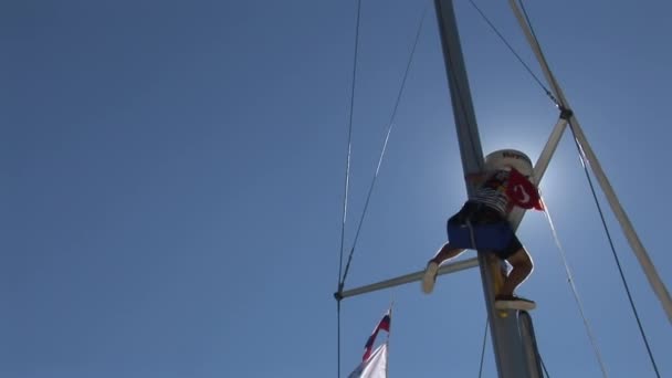 Man zit op mast van jacht op de achtergrond van blauwe lucht en zon . — Stockvideo