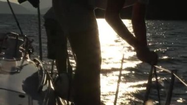 Beyaz şapkalı ve beyaz tişörtlü adam beyaz yelkenli yatta vinç ve ipleri çeviriyor..