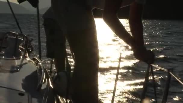 Man in white cap and white T-shirt turns winch and ropes on yacht with white sails. — Stock Video