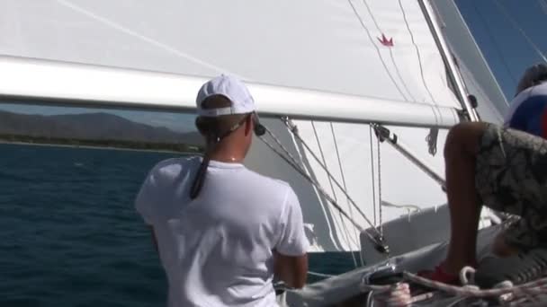 Två män på däck av yacht med vita segel arbetar med rep på yacht. — Stockvideo